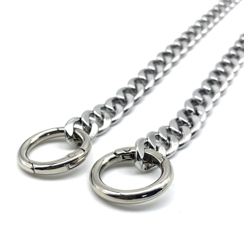 May include: A silver chain with two silver clasps. The chain is thick and has a curb link design.