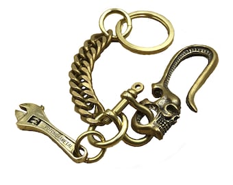 May include: A brass keychain with a skull hook, a wrench charm, and a chain link. The wrench charm has the text "POTONG AMETAL" engraved on it.