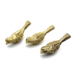 Könnte beinhalten: Drei goldfarbene Vogelfiguren aus Metall. Die Vögel sind in verschiedene Richtungen gewandt und haben detaillierte Texturen.
