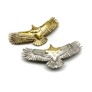Op de afbeelding: Twee adelaar hangers, een gouden en een zilveren, met wijd uitgespreide vleugels. Beide hangers zijn versierd met ingewikkelde gravures.