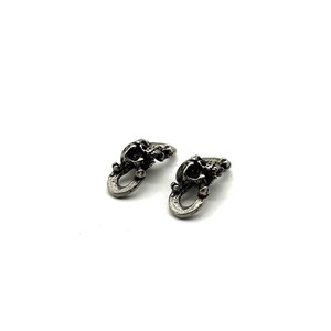 May include: Two small, silver-toned skull-shaped charms. Each charm features a detailed skull design with an open loop at the bottom. The charms are displayed against a white background.