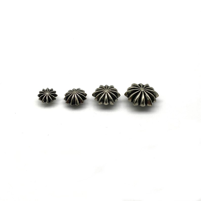 May include: Four silver star-shaped studs of varying sizes. The studs have a raised, textured design.