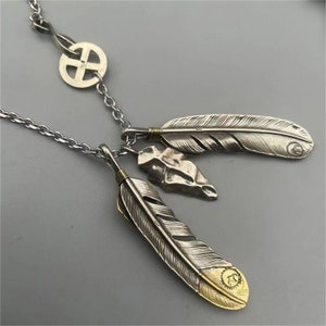 May include: Silver necklace with a cross pendant and three feather charms. The feathers are detailed with intricate designs and have a gold accent.