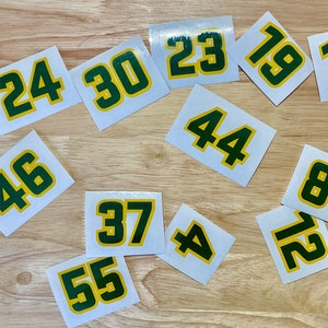 May include: A collection of white square stickers with various numbers in green, outlined in yellow. The numbers include 24, 30, 23, 19, 13, 46, 44, 8, 12, 37, 55, and 4. The stickers are arranged on a light wood surface.