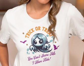 以下が含まれることがあります： ハロウィーンをテーマにしたグラフィックの白いTシャツ。デザインは、青い髪の漫画の幽霊、「トリック・オア・トリート」というテキスト、そして「You Can't Scare Me I Have Kids!」というフレーズを紫で表示しています。