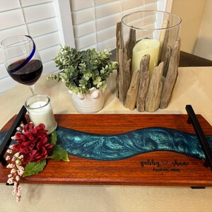 May include: A wooden serving tray with a teal blue epoxy river design. The tray has black metal handles and is personalized with the names "Gabby & Shane" and the date "Aug 28, 2022".