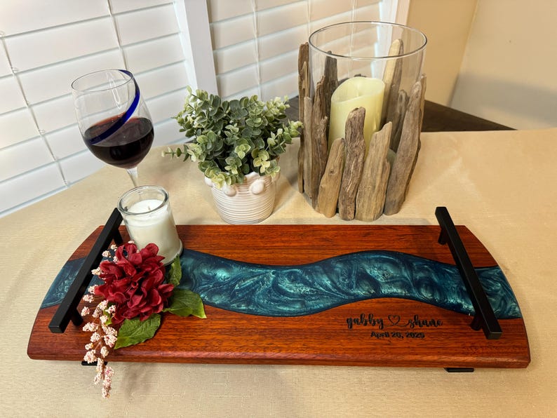 May include: A wooden serving tray with a teal blue epoxy river design. The tray has black metal handles and is personalized with the names "Gabby & Shane" and the date "Aug 28, 2022".