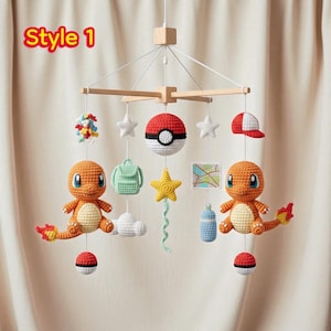May include: A handmade baby mobile featuring crocheted Pokémon-themed characters and accessories. The mobile includes two orange Charmander figures, a Pokéball, stars, a backpack, a map, a bottle, a cloud, a yellow star, and a baseball cap. The text "Style 1" is visible.