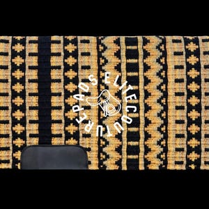 May include: A rectangular horse saddle pad with a black and gold geometric pattern. The pad features a black leather-like bottom and the text "UPPER ELITE PADS COUTURE" in a circular design in the centre.