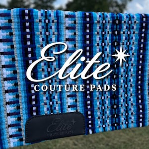 May include: A blue and white patterned saddle pad with the text "Elite Couture Pads". The pad has a rectangular shape with a dark leather patch at the bottom. The design features various shades of blue and white.