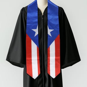 May include: A black graduation gown with a blue and red sash featuring the Puerto Rican flag. The sash has a white star on each side.