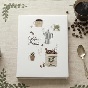 May include: A white notebook with embroidered coffee-themed illustrations, including a coffee pot, cups, and coffee beans. The words "Coffee Break" are written in cursive. A cup of coffee, coffee beans, and a spoon are also present.