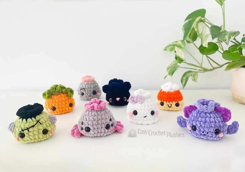 May include: A collection of small, handmade crochet plushies in various shapes and colors, including a green monster, orange pumpkin, grey creature, black blob, white ghost, candy corn, and purple monster, with the text Easy Crochet Plushies.