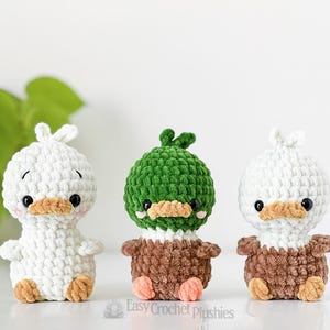 May include: Three handmade crochet duck plushies. One is white, one is green, and one is white. Each has a brown beak and feet, and black eyes. The green duck has a green head and brown body. The white ducks have white heads and brown bodies.