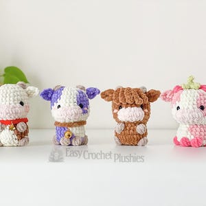 May include: Four handmade crochet cow plushies in various colours: brown and white, purple and white, brown, and pink and white. Each plush has a unique design, including bells and a strawberry-like top. The text "Easy Crochet Plushies" is visible.