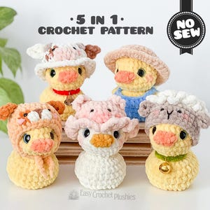 May include: Five crochet duck plushies, each wearing a different animal hat: cow, pig, bear, sheep, and duck. The ducks are yellow with orange beaks and black eyes. The hats are various colours, including pink, brown, and white. The text "5 in 1 Crochet Pattern" is at the top.