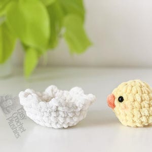 May include: A crocheted yellow chick with a peach beak and black eyes sits beside a white crocheted bowl. The chick has rosy cheeks. The bowl is round with a ruffled edge. The text "Easy Crochet Plushies" is visible.