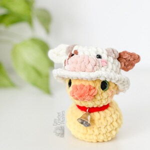 Op de afbeelding: Een handgemaakte gele gehaakte eend met een koeienhoed met bruine en witte accenten. De eend heeft een rode kraag met een kleine zilveren bel. De knuffel is een grillige creatie, perfect voor een kinderkamer of als uniek cadeau.