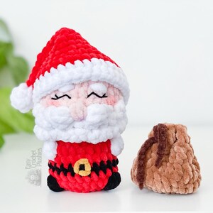May include: A crocheted Santa Claus plushie with a red hat and suit, white beard and trim, and a black belt with a gold buckle. A small brown sack is next to the Santa plushie. The text "Easy Crochet Plushies" is on the side.