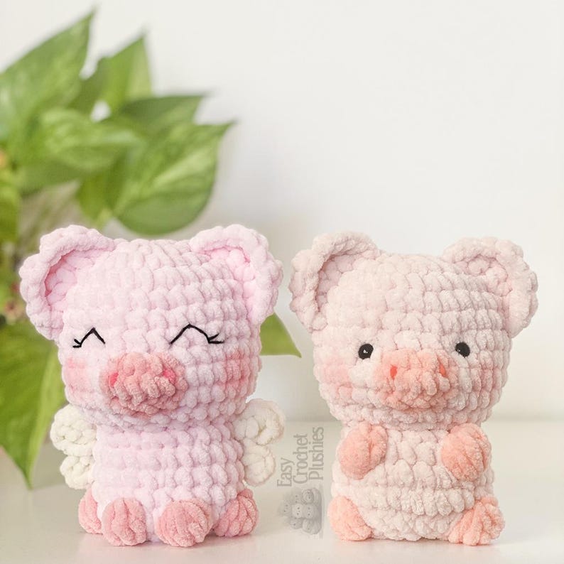 May include: Two handmade crochet pig plushies in shades of pink. One pig has closed eyes, blush, and small white wings. The other pig has open eyes and blush. The text "Easy Crochet Plushies" is visible on the right.