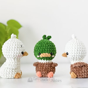 Peut inclure: Trois petites peluches au crochet repr&eacute;sentant un canard blanc, un colvert &agrave; t&ecirc;te verte et corps brun, et un canard blanc et brun. Chaque peluche a des yeux en perles noires, un petit bec et le texte Easy Crochet Plushies est visible en dessous.