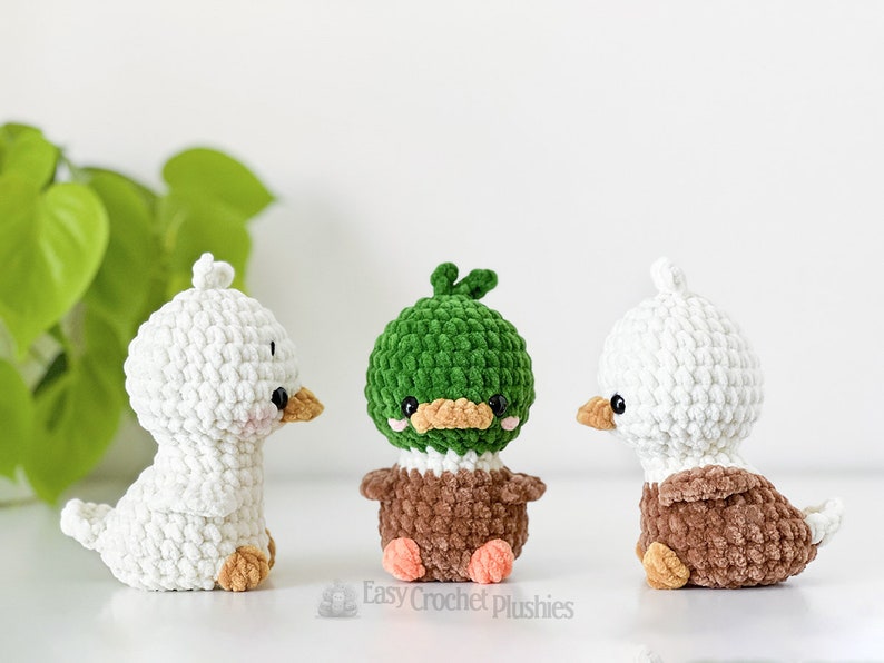 Peut inclure: Trois petites peluches au crochet repr&eacute;sentant un canard blanc, un colvert &agrave; t&ecirc;te verte et corps brun, et un canard blanc et brun. Chaque peluche a des yeux en perles noires, un petit bec et le texte Easy Crochet Plushies est visible en dessous.