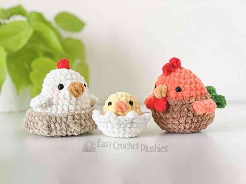 May include: Three crocheted plush chickens. A white chicken sits in a tan nest, a yellow chick peeks from a white eggshell, and a brown and orange chicken stands. The text "Easy Crochet Plushies" is at the bottom of the image.
