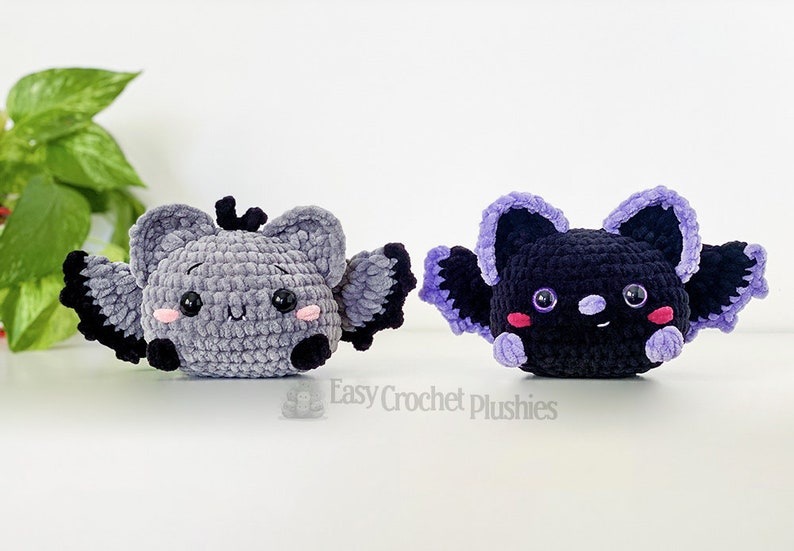 Puede incluir: Dos murci&eacute;lagos de peluche tejidos a crochet, uno gris con alas moradas y otro negro con alas moradas. Ambos murci&eacute;lagos tienen ojos negros y mejillas rosadas.