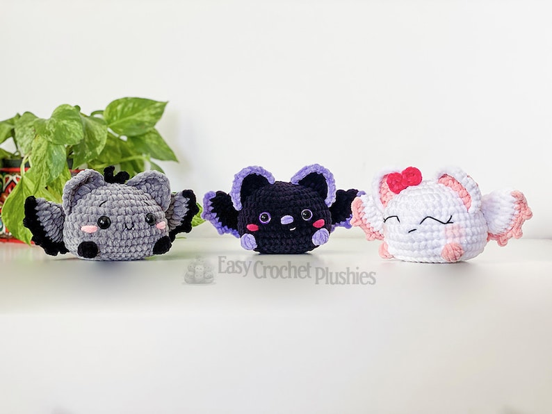 Puede incluir: Tres murci&eacute;lagos de peluche tejidos a crochet en diferentes colores. El murci&eacute;lago de la izquierda es gris con ojos negros y una nariz rosa. El murci&eacute;lago del medio es negro con alas moradas y mejillas rosadas. El murci&eacute;lago de la derecha es blanco con alas rosadas y un lazo rosa. Easy Crochet Plushies.