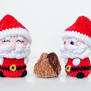 May include: Two crochet Santa Claus plushies with red hats and suits, white beards, and black belts with gold buckles. A small brown plushie is between them. The plushies are handmade and suitable for Christmas.