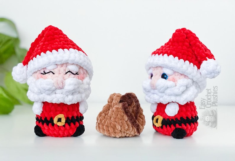 May include: Two crochet Santa Claus plushies with red hats and suits, white beards, and black belts with gold buckles. A small brown plushie is between them. The plushies are handmade and suitable for Christmas.