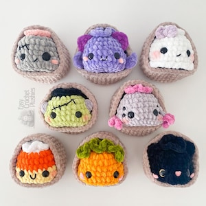 May include: Eight small, round, crocheted plushies in individual tan yarn baskets. The plushies feature various designs including a grey monster, purple creature, white ghost, green Frankenstein-like figure, grey spider, candy corn, pumpkin, and black cat.