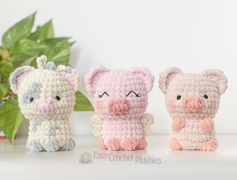 May include: Three handmade crochet plushies: a cow, and two pigs. The cow is white with grey and pink accents. The pigs are pink with embroidered details. The plushies are soft and cuddly, ideal for children.