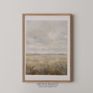 Op de afbeelding: Een ingelijste landschapskunstafdruk met een veld met hoog gras onder een bewolkte lucht. Het kunstwerk heeft een gedempte kleurenpalet van beige, grijs en blauw. De lijst is lichtbruin. De tekst "ARTISAN REALITY classic printable art" staat onderaan.
