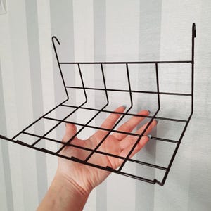 Può includere: Mensola in filo metallico nero con motivo a griglia. La mensola è progettata per essere appesa a una parete.