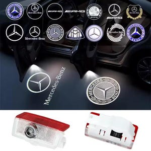 Op de afbeelding: Afbeelding met Mercedes-Benz autodeurprojectorlampen en logo's. De afbeelding toont verlichte logo's, waaronder het Mercedes-Benz embleem, AMG en Maybach logo's. De lichten projecteren op de grond, en er zijn ook twee projectorlichteenheden.