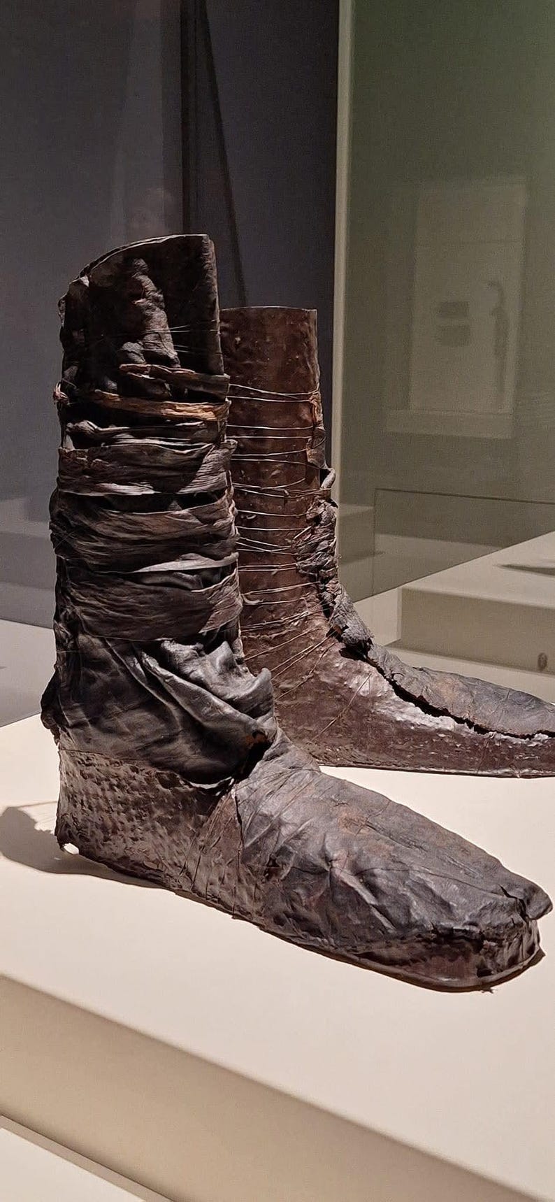 May include: A pair of brown leather boots with a unique design. The boots are made of multiple layers of leather, which have been stitched together. The boots are on display in a museum.