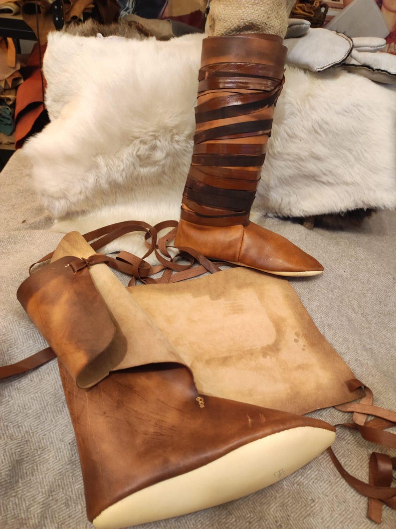 May include: A pair of brown leather boots with laces. The boots are made of thick leather and have a pointed toe. The boots are sitting on a white fur rug.