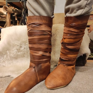 May include: Brown leather boots with a wraparound design. The boots are tall and have a pointed toe.