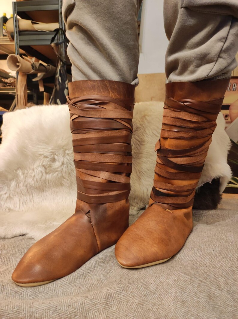 May include: Brown leather boots with a wraparound design. The boots are tall and have a pointed toe.
