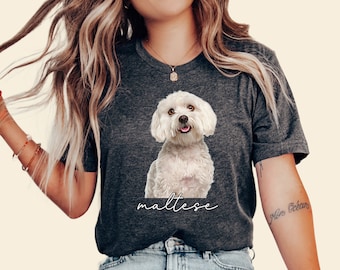 May include: A dark gray t-shirt with a white Maltese dog graphic and the word "maltese" written in white script below the dog. The model is wearing the shirt and has long blonde hair.