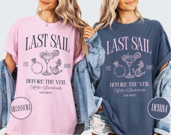 May include: Two t-shirts, one pink and one navy blue, each with the text "LAST SAIL" and "BEFORE THE VEIL". The design includes a cocktail, ring, and anchor. The pink shirt has "BLOSSOM" and the navy shirt has "DENIM" in a circle.