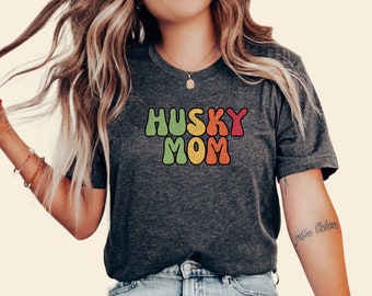 May include: A dark grey t-shirt with the text "HUSKY MOM" in a retro rainbow font.