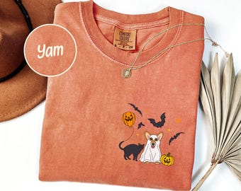 May include: A coral-colored t-shirt with a Halloween-themed graphic. The design includes a black cat, a dog in a ghost costume, bats, and jack-o'-lanterns. The word "Yam" is in a circle in the upper left corner.