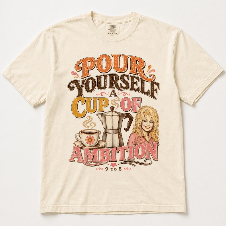 May include: A cream-colored short-sleeve t-shirt featuring a graphic print with the text "POUR YOURSELF A CUP OF AMBITION" and "9 TO 5". The design includes a coffee cup, a moka pot, and an illustration of a blonde person in a pink shirt.