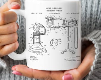 Op de afbeelding: Een witte keramische mok met een zwart-witte illustratie van een patent voor een anesthesiemachine. Het patent is gedateerd 5 augustus 1919 en is getiteld "United States Patent, Anesthesiemachine, J.G.E. Hinkle, Pat. 1,312,117".