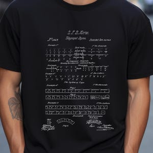 May include: Black t-shirt featuring a white diagram of S.F.B. Morse's telegraph signs, including examples of numerals and letters. The diagram is a patent illustration with detailed technical drawings and text.