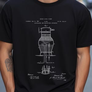 Può includere: T-shirt nera con un diagramma bianco di un apparato di distillazione e rettifica. Il diagramma include disegni tecnici e testo che dettaglia le informazioni sul brevetto, l'inventore e i testimoni. La maglietta ha un girocollo.
