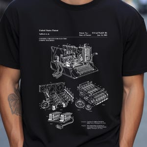 Puede incluir: Camiseta negra con un diagrama técnico blanco de una máquina de codificación. El diagrama incluye texto que indica una patente de Estados Unidos, el número de patente US 6.175.625 B1 y la fecha del 16 de enero de 2001. El diseño muestra los intrincados componentes internos.