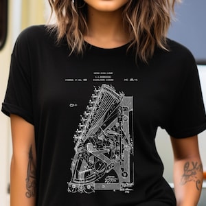 May include: Black t-shirt featuring a white print of a vintage patent drawing for a mechanical device. The drawing includes text that reads "UNITED STATES PATENT, J.L. NORRIS,  TYPEWRITER,  PAT. 386,115".